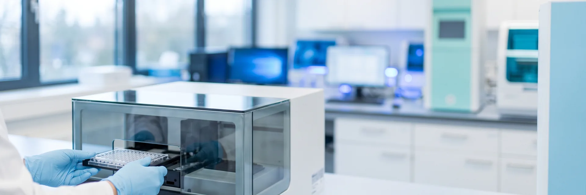 Behandschuhte Hände setzen eine Probenplatte in ein Laborgerät ein